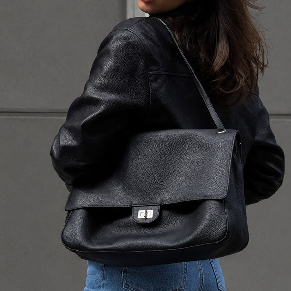 Structured black flap shoulder bag with pebbled texture, silver-tone turn-lock closure, and adjustable single shoulder strap