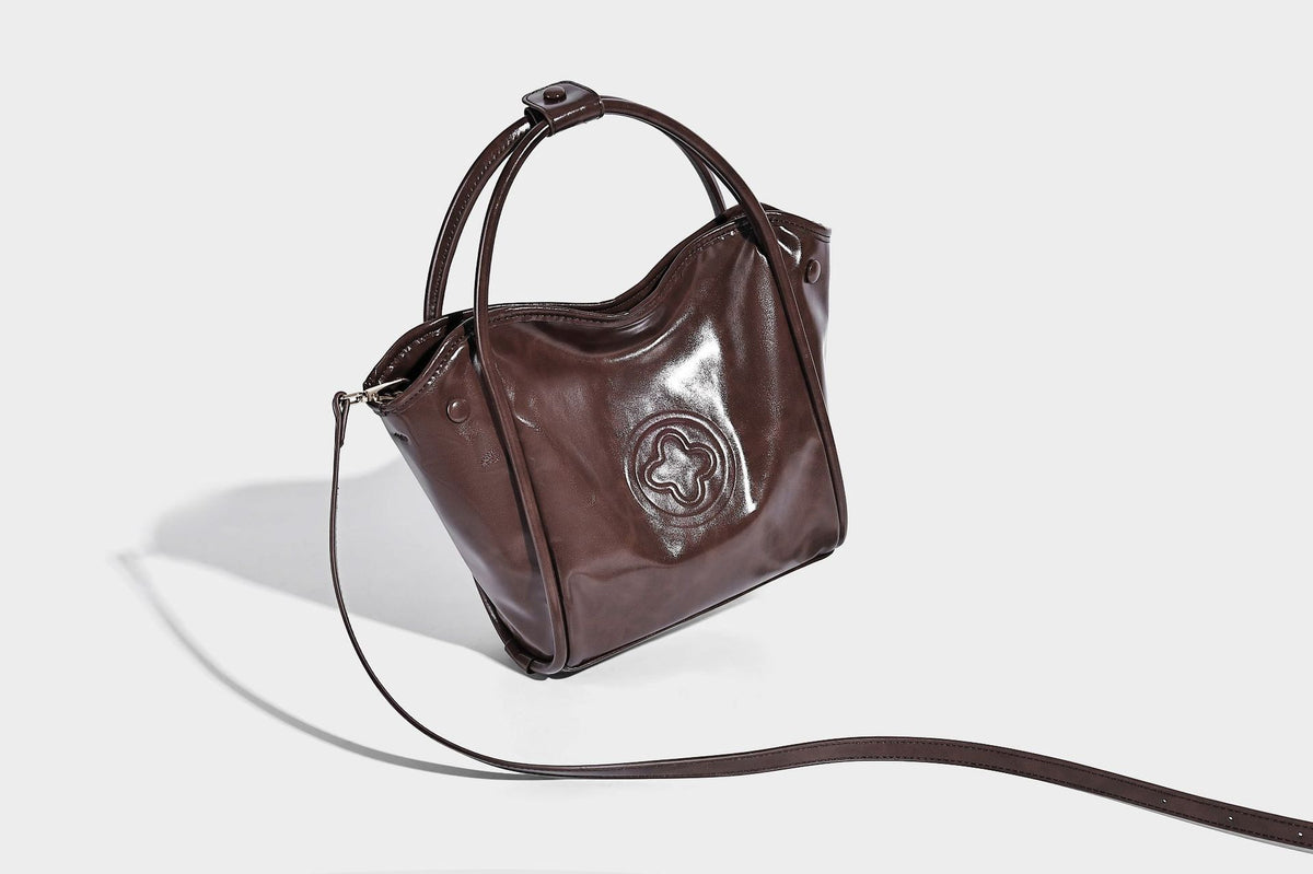 Glossy leather-look structured tote bag with rounded top handles, detachable shoulder strap, embossed front emblem, and side