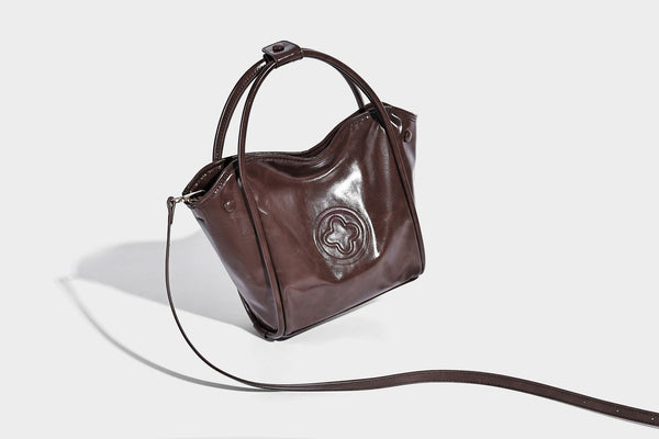 Glossy leather-look structured tote bag with rounded top handles, detachable shoulder strap, embossed front emblem, and side