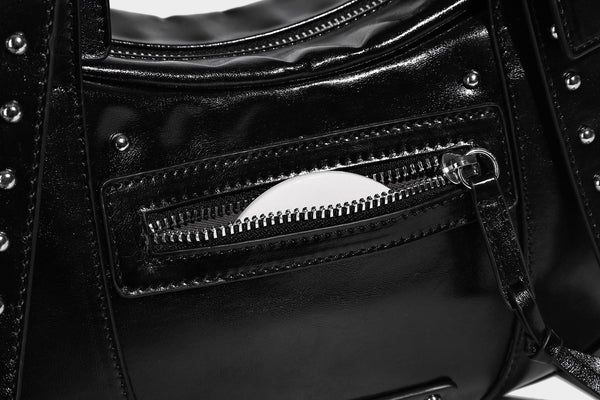 Glossy black crescent shoulder bag with silver-tone rivets, multiple zip pockets, and long adjustable studded straps, detail