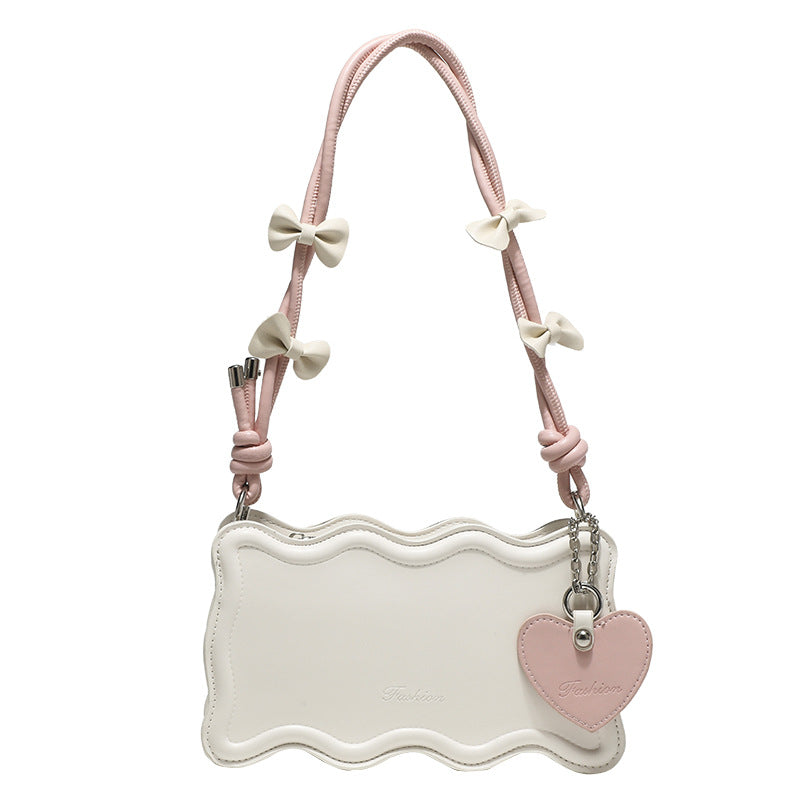 Small structured scalloped-edge shoulder bag with bow-tied pink cord strap and silver heart charm pendant, detail view 5