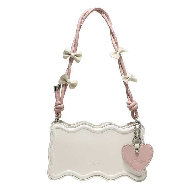 Small structured scalloped-edge shoulder bag with bow-tied pink cord strap and silver heart charm pendant, detail view 5
