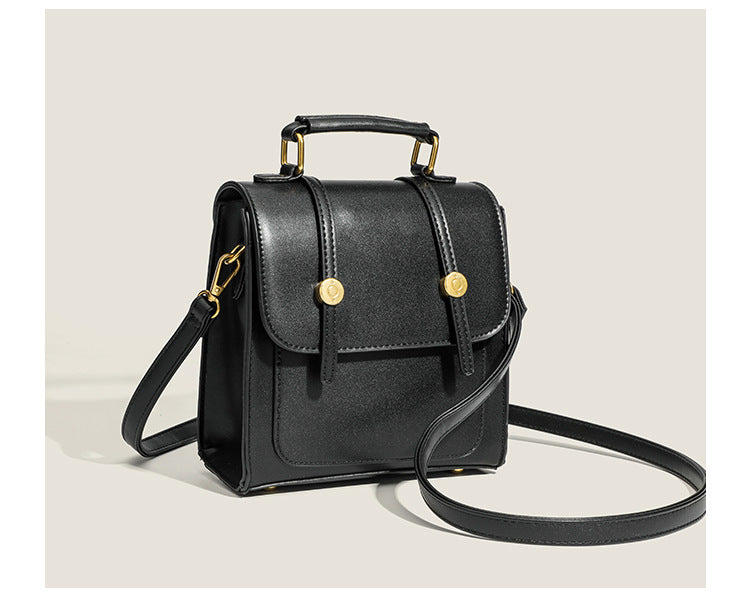 Structured mini satchel backpack with smooth leather-look finish, front flap pocket, gold-tone stud closures, and top handle