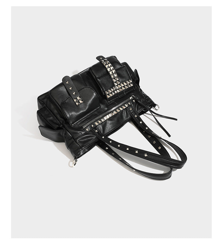 Black leather-look tote bag with silver pyramid studs on handles and front panel, multiple flap and zip exterior pockets