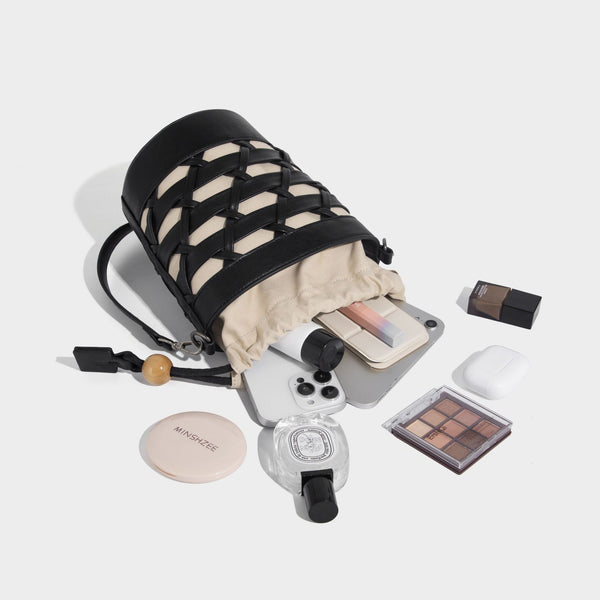 Small cylindrical woven lattice bucket bag with leather-look black trim, beige canvas body, wooden bead drawstring closure