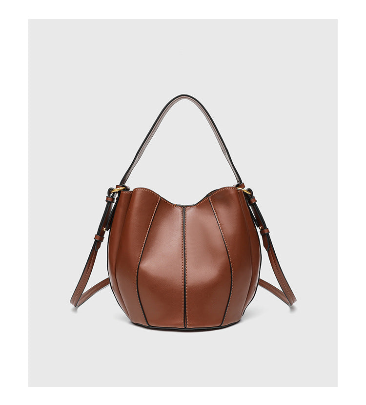 Smooth leather-look paneled bucket bag in brown with wide woven shoulder strap, gold-tone ring hardware, and detachable zip