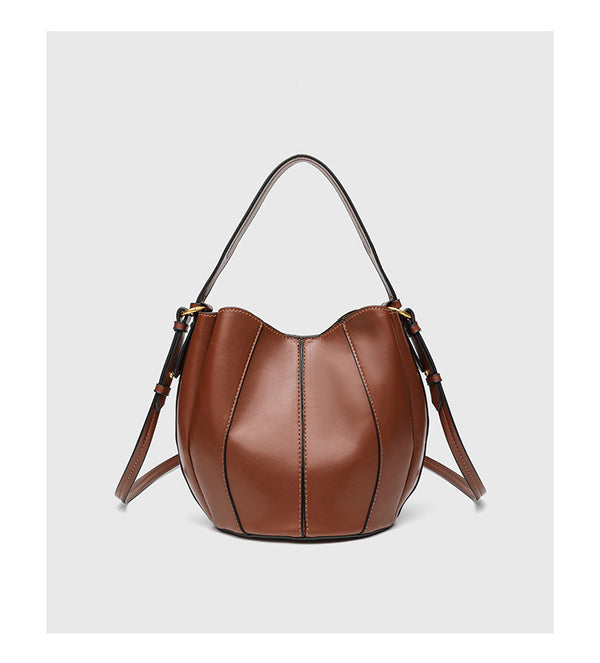 Smooth leather-look paneled bucket bag in brown with wide woven shoulder strap, gold-tone ring hardware, and detachable zip