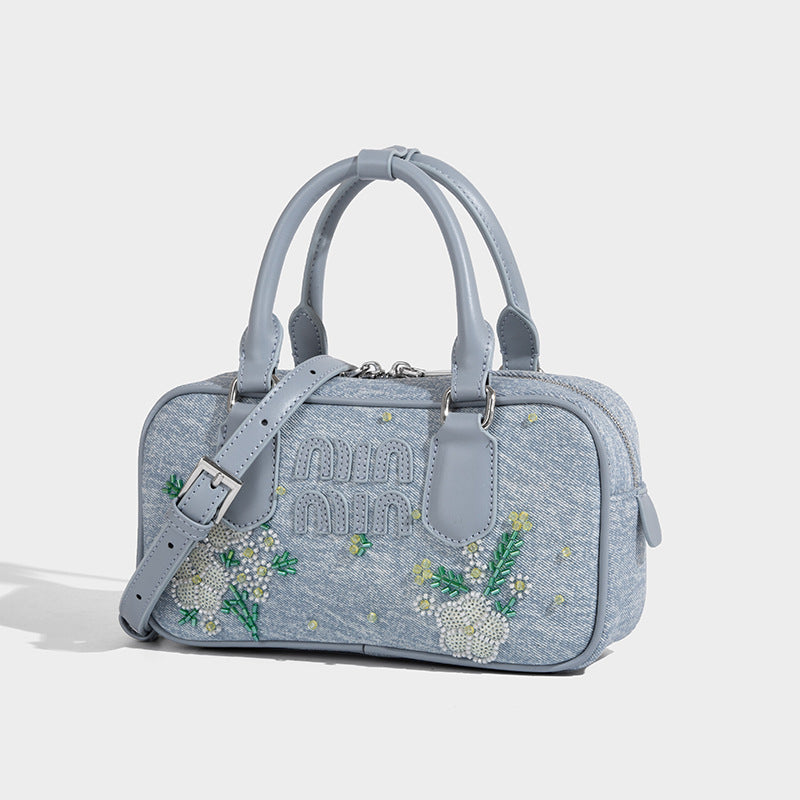 Small light blue denim-look barrel bag with white floral bead embroidery, dual top handles, and detachable shoulder strap