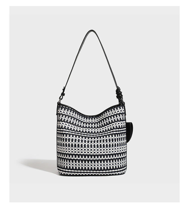 Woven stripe bucket shoulder bag in cream and dark brown with leather-look trim, knotted adjustable strap, and small shield