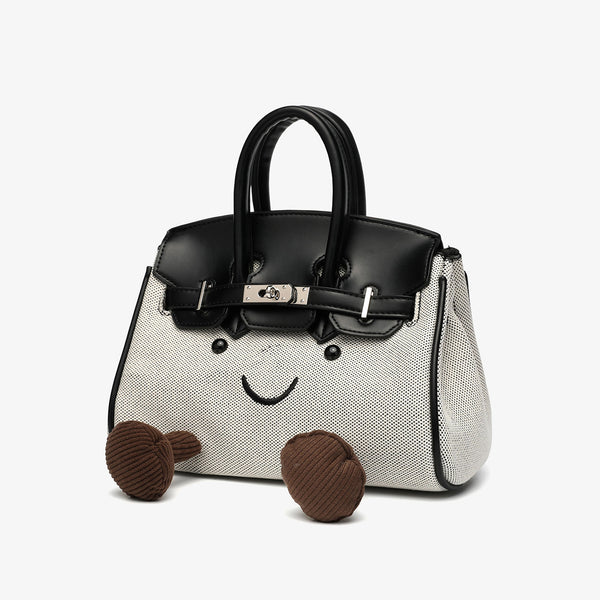 Small structured trapezoid satchel bag with smiling face motif, pom-pom accents, brown leather-look trim, silver-tone, detail