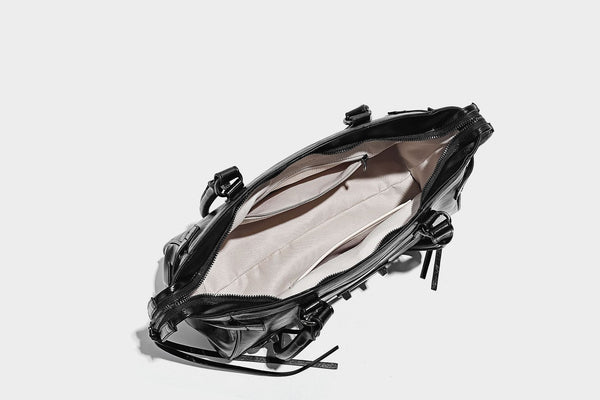 Längliche Schultertasche in Zylinderform mit glänzender Lederoptik, silberfarbenen Nietenbeschlägen, seitlichen Quasten und mehreren außenliegenden Reißverschlüssen