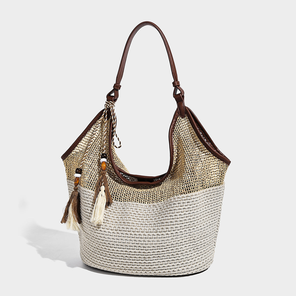 Two-tone beige and cream woven straw hobo shoulder bag with brown leather-look trim, long shoulder strap, and tassel-bead