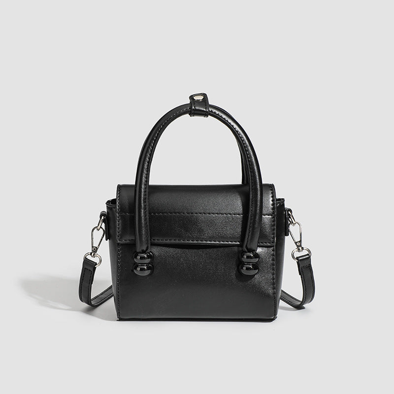 Kleine strukturierte schwarze Henkeltasche im Lederlook mit zwei abgerundeten Henkeln, abnehmbarem Umhängeriemen und silberfarbenem