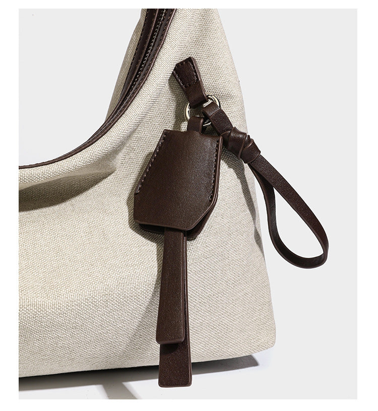 Lässig geschnittene Hobo-Schultertasche aus Canvas in Haferflockenfarbe mit dunkelbraunem Besatz in Lederoptik, silberfarbenem Reißverschluss und langem, verstellbarem