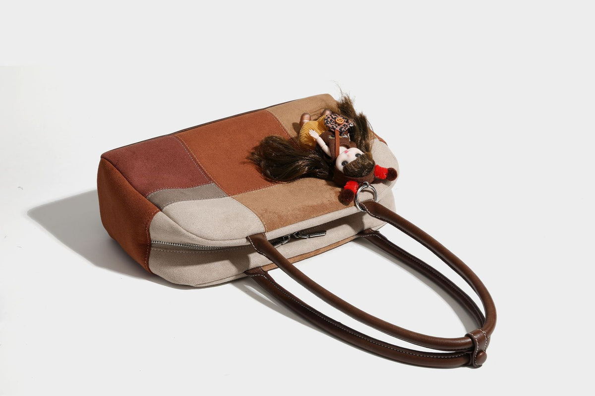 Boxy patchwork suede-look shoulder tote in tan, beige, rust, and brown panels with double brown straps and hanging doll