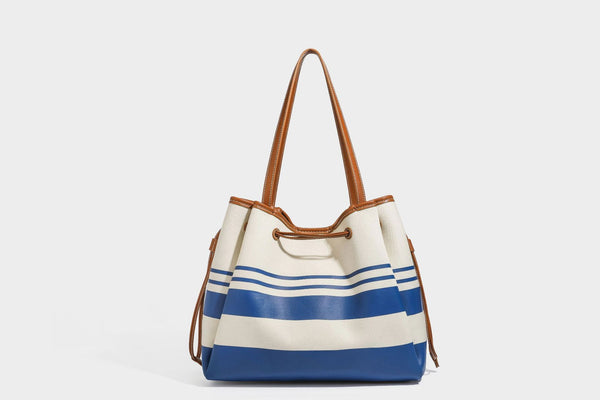 Large cream and navy striped canvas bucket tote bag with tan leather-look trim, drawstring closure, and double shoulder