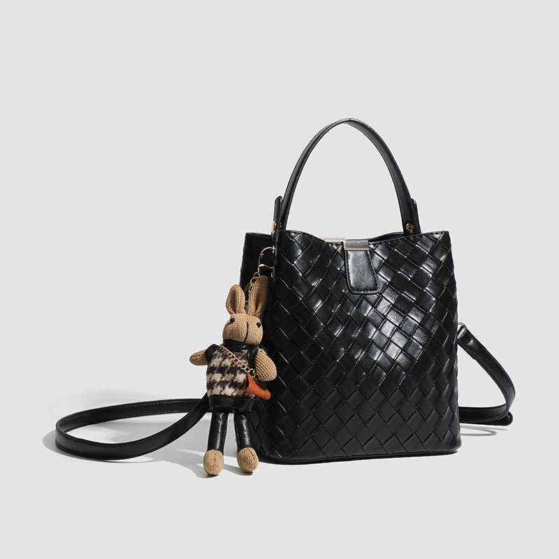 Black woven leather-look bucket bag with gold-tone clip closure, top handle, detachable shoulder strap, and knit bunny charm