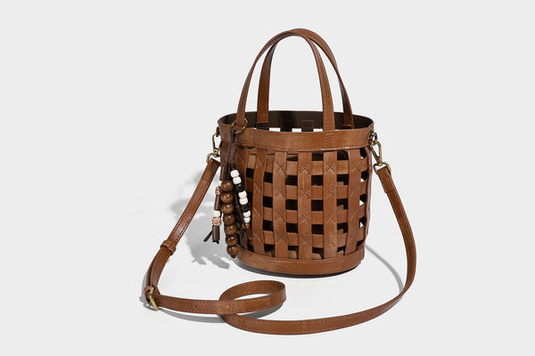 Small woven lattice bucket bag in brown leather-look finish with beaded tassel charm, dual top handles, and detachable