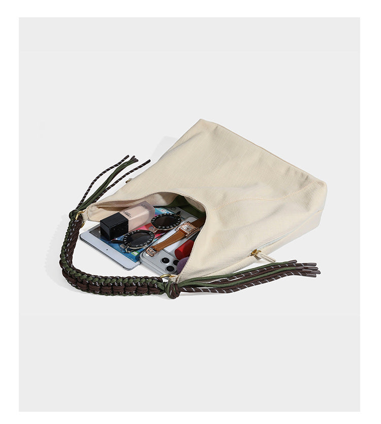 Soft slouchy cream canvas shoulder tote with braided brown and green cord handle, gold-tone ring hardware, and tassel trim