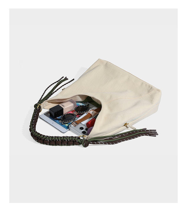 Soft slouchy cream canvas shoulder tote with braided brown and green cord handle, gold-tone ring hardware, and tassel trim