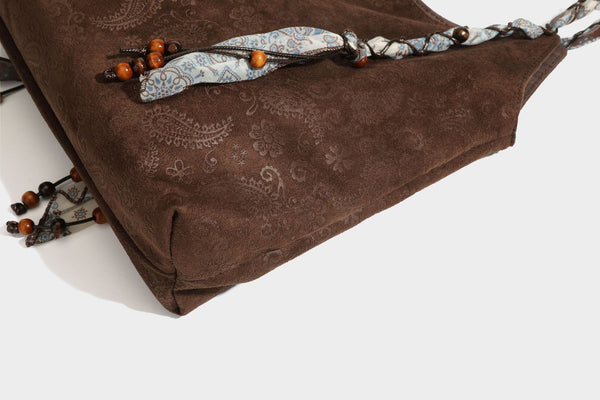 Slouchy paisley-embossed suede-look shoulder tote bag with braided patterned fabric straps and wood bead accents, detail view