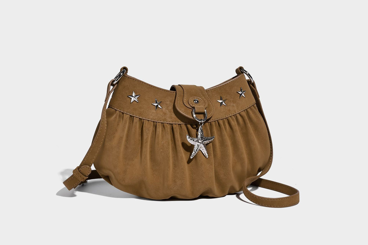 Ruched shoulder bag with curved flap, silver star studs, dangling starfish charm, and adjustable crossbody strap, detail view