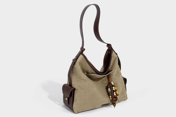 Lässig fallende Hobo-Schultertasche in Khaki aus mattem Material in Wildlederoptik mit dunkelbraunem Besatz in Lederoptik, Quastenanhänger mit Perlen und seitlicher Klappe, Detailansicht