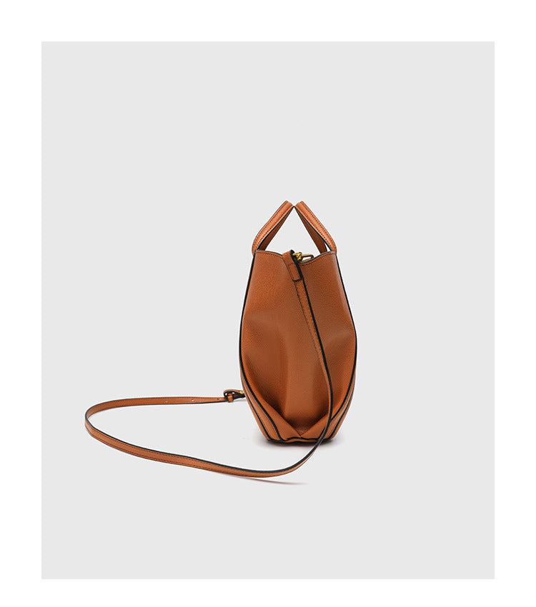 Structured open-top tote bag in tan brown pebbled leather-look finish with vertical seam accents, black edge piping, curved