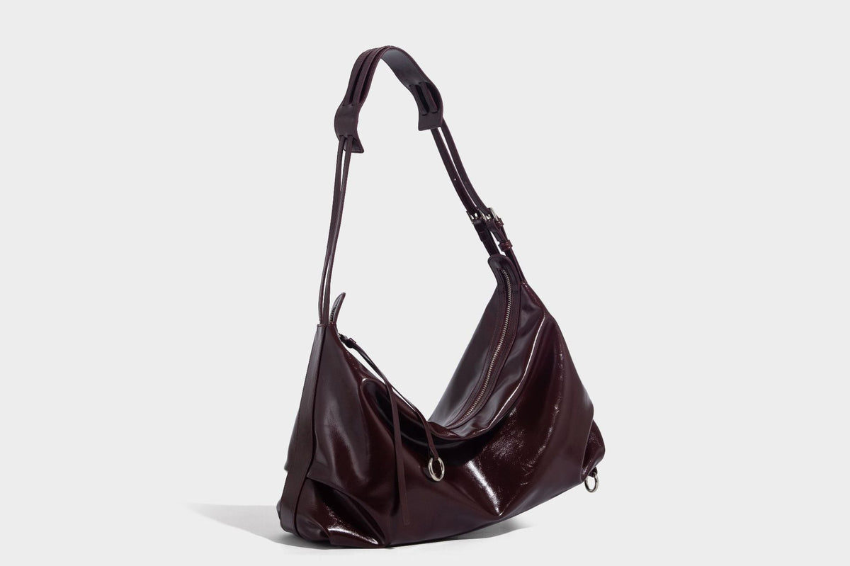 Glossy black slouchy hobo shoulder bag with zip closure, silver-tone ring hardware, and adjustable crossbody strap, detail