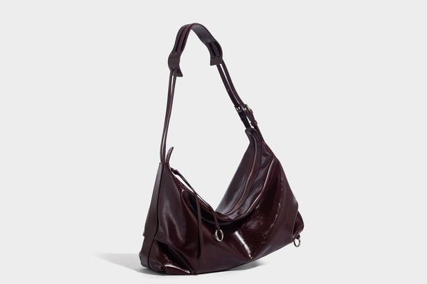 Glossy black slouchy hobo shoulder bag with zip closure, silver-tone ring hardware, and adjustable crossbody strap, detail