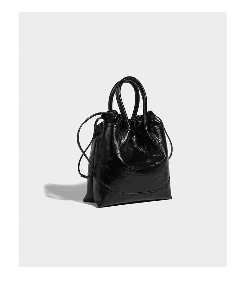 Glossy crinkled ruched drawstring bucket bag with rounded double top handles and detachable chain crossbody strap, detail