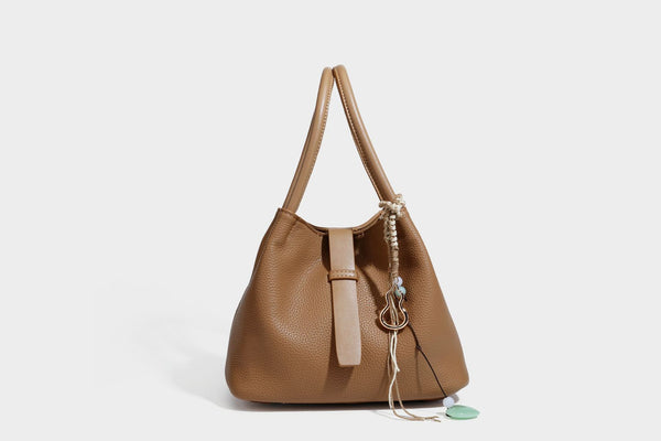 Pebbled leather-look bucket tote bag with rolled double handles, drawstring closure, braided cord charm, and detachable