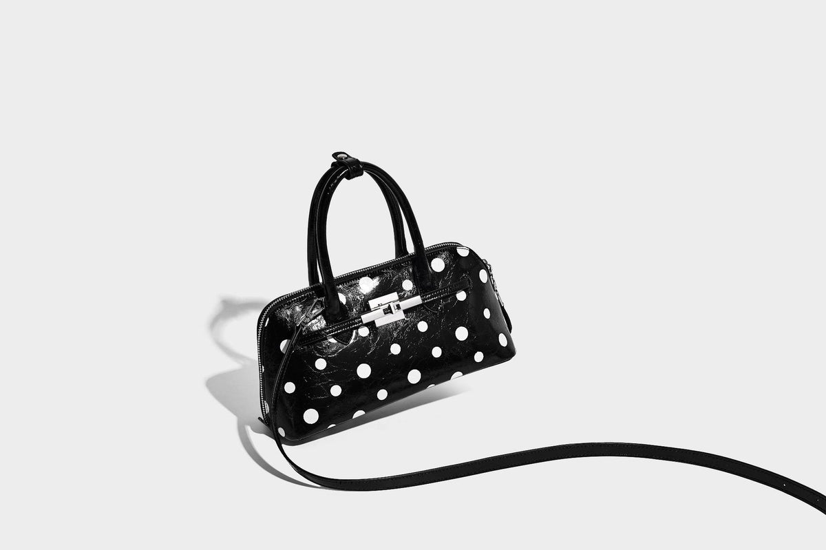 Glossy structured polka-dot satchel bag with dual top handles, silver turn-lock hardware, and detachable shoulder strap