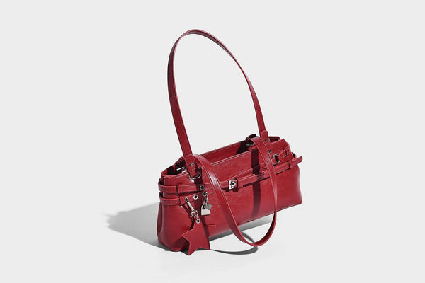 Structured glossy leather-look shoulder bag with wraparound belt straps, silver-tone hardware, and dangling star charm