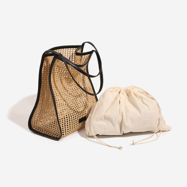Tan open-weave raffia tote bag with black leather-look trim and long black shoulder straps, trapezoid silhouette, detail view