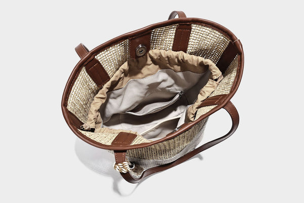 Woven straw-look tote bag in tan and cream with dark brown leather-look trim, long flat shoulder straps, and tassel bead