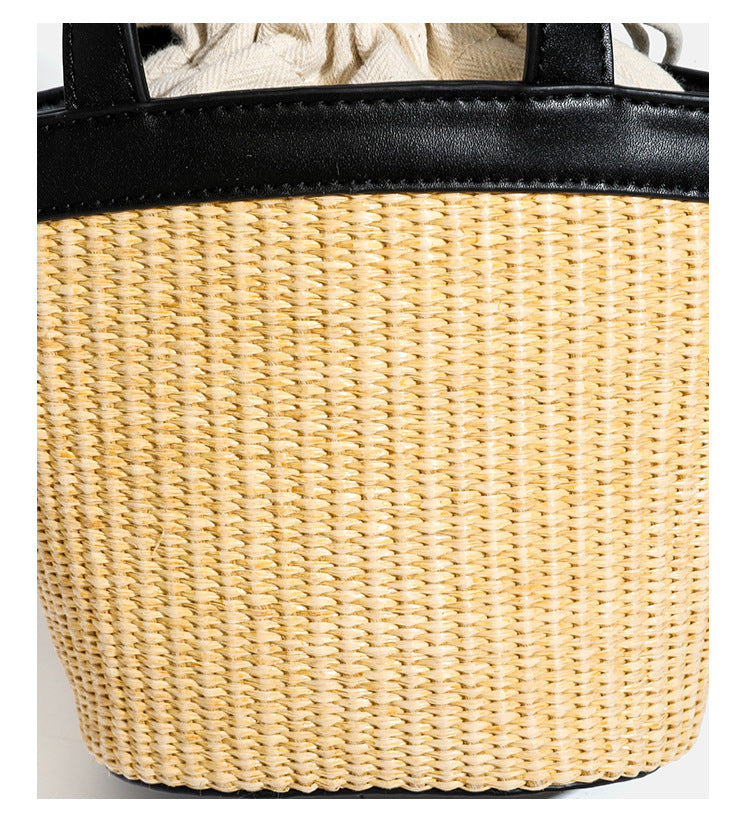 Kleine geflochtene Bucket Bag aus Stroh mit schwarzem Besatz in Lederoptik, zwei oberen Tragegriffen, cremefarbenem Futter mit Kordelzug und seitlichen Kordelverschlüssen