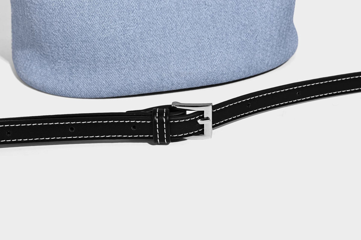 Hellblaue Bucket-Bag aus Denim mit schwarzem Besatz in Lederoptik, silberfarbenen Beschlägen, kurzem Tragegriff und langem verstellbarem Crossbody-Riemen