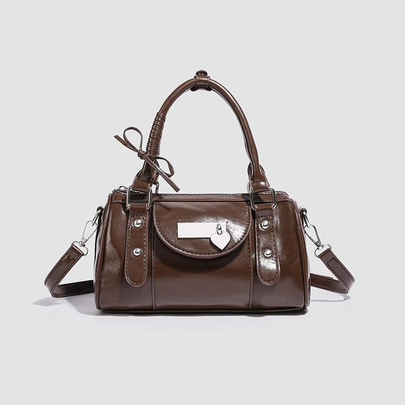 Small structured barrel handbag in glossy leather-look finish with bow-accented top handles, heart-clasp front pocket, front