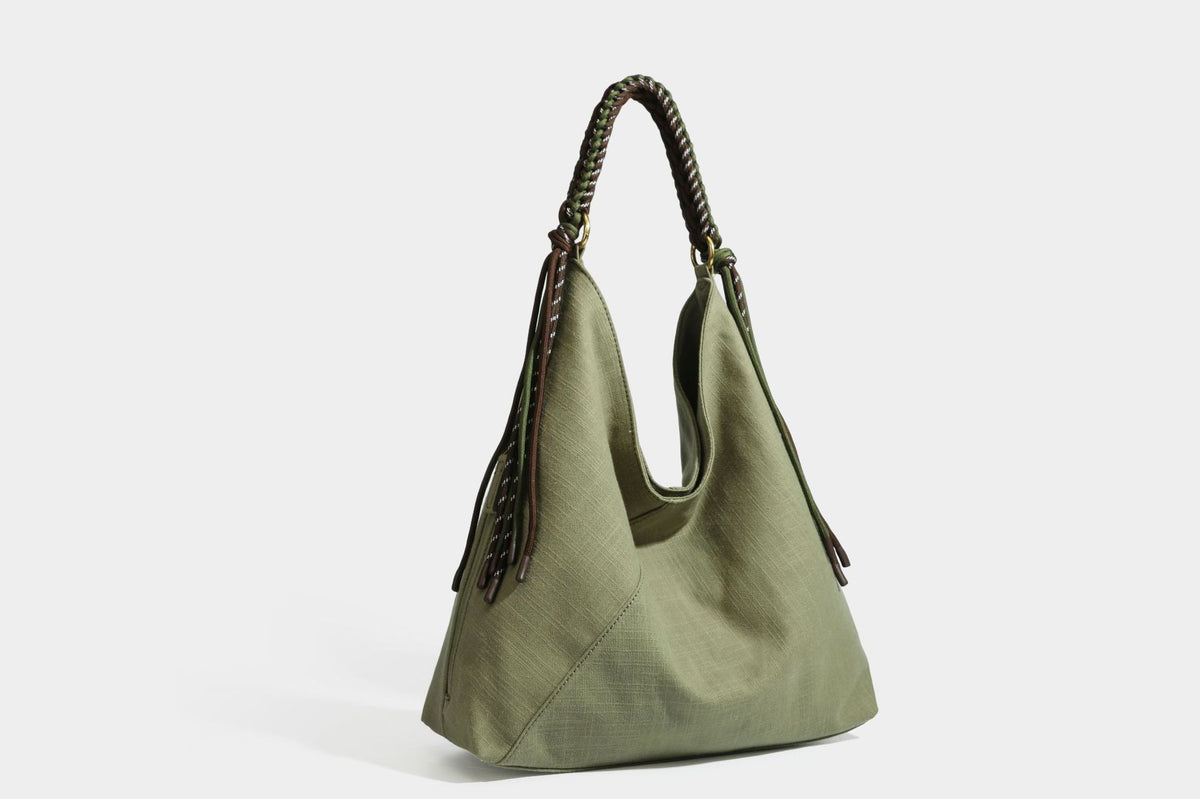 Soft slouchy cream canvas shoulder tote with braided brown and green cord handle, gold-tone ring hardware, and tassel trim