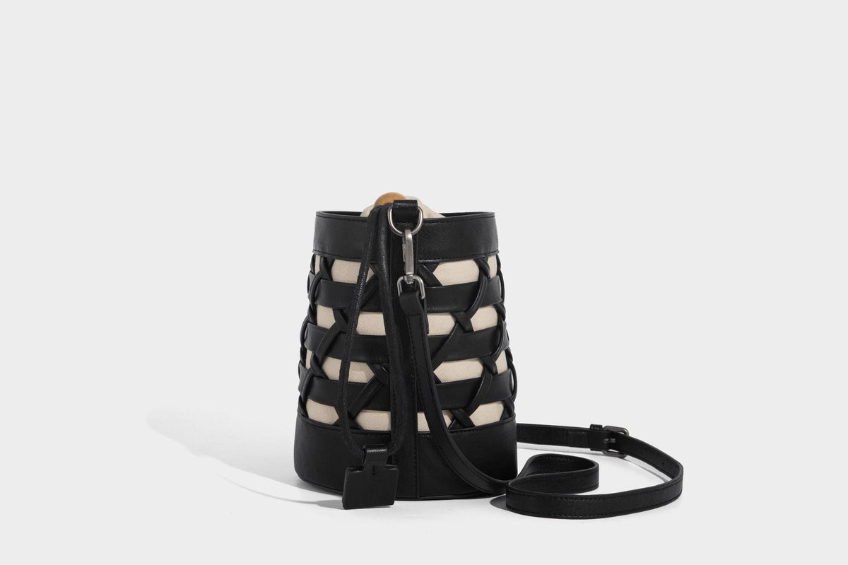 Small cylindrical woven lattice bucket bag with leather-look black trim, beige canvas body, wooden bead drawstring closure