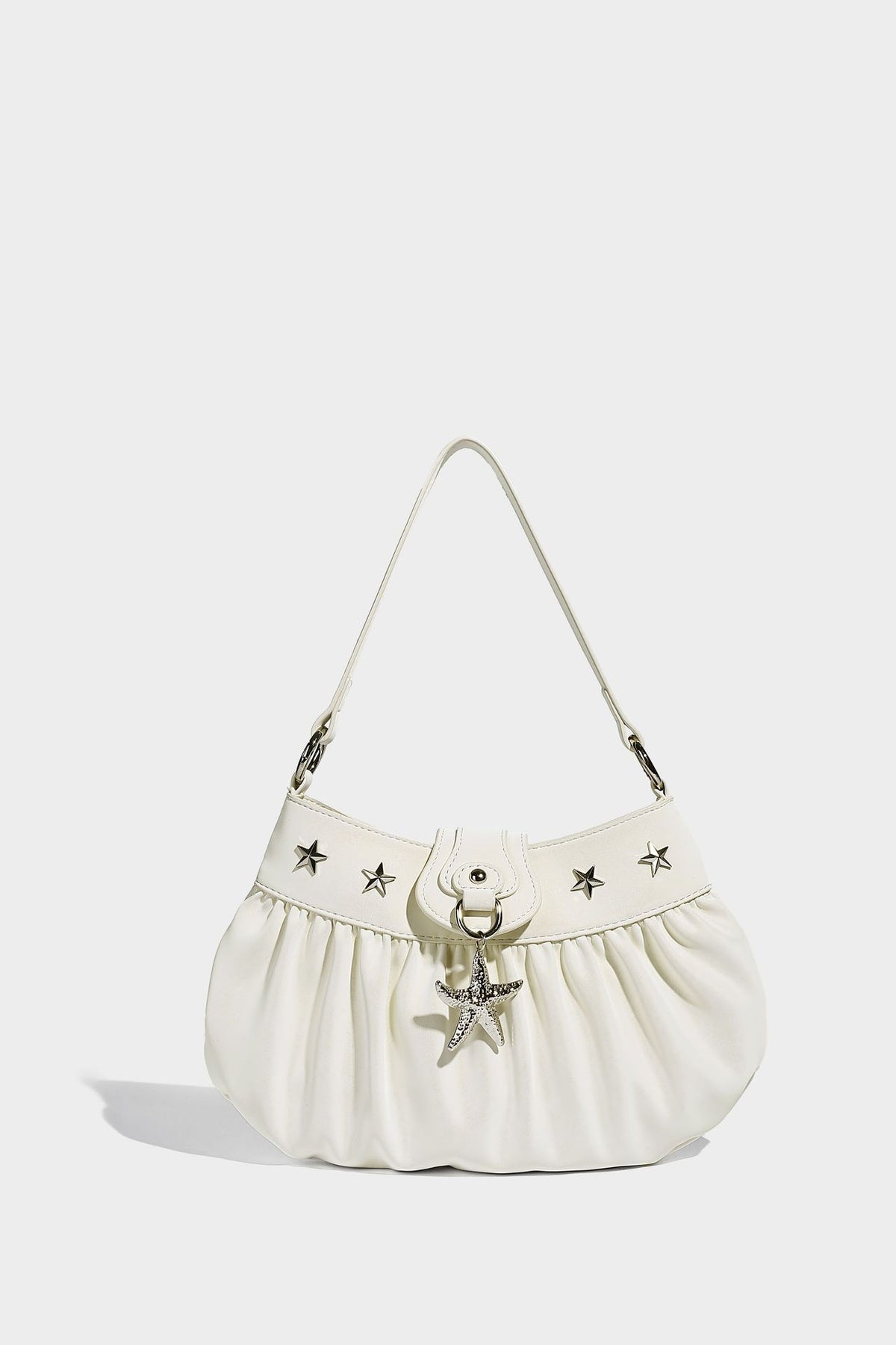 Ruched shoulder bag with curved flap, silver star studs, dangling starfish charm, and adjustable crossbody strap, detail view