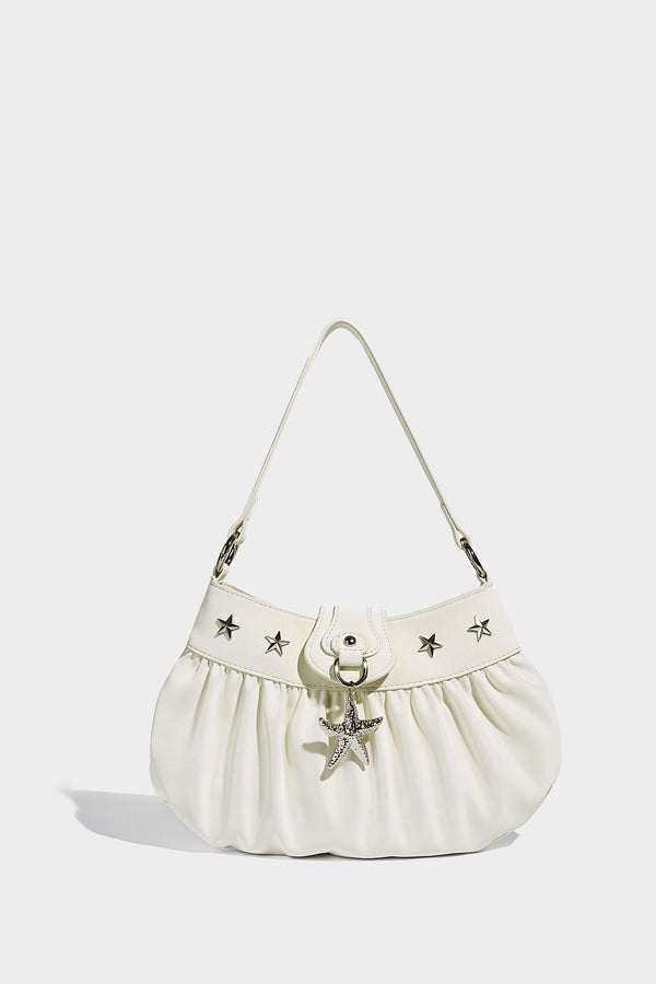 Ruched shoulder bag with curved flap, silver star studs, dangling starfish charm, and adjustable crossbody strap, detail view