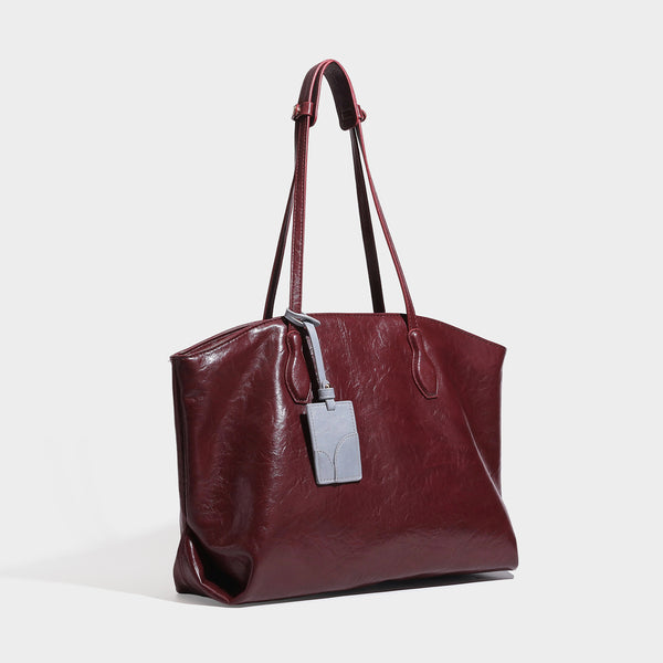 Oversized-Shopper mit lässig-weicher Form in dunkler Burgunderfarbe, glänzender geknautschter Lederoptik, zwei langen Schulterriemen und kontrastierendem