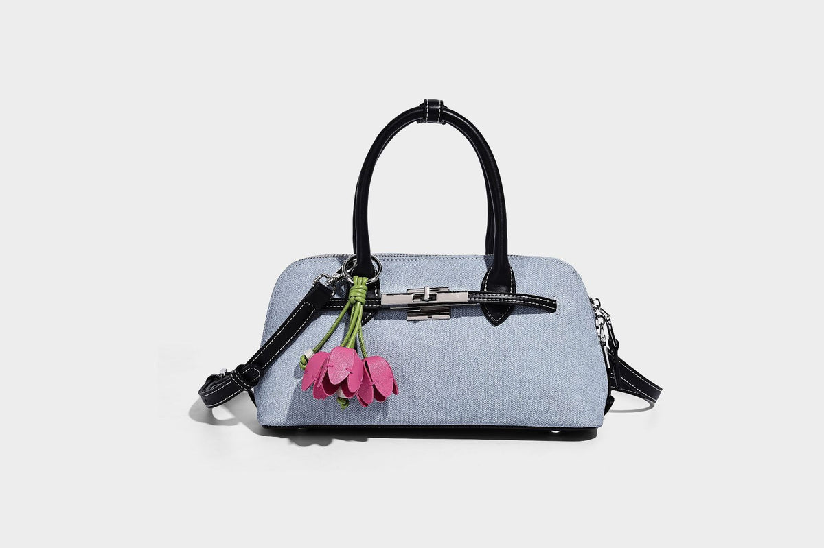Compact structured satchel in light blue denim-look fabric with black leather-look trim, silver turn-lock closure, rolled