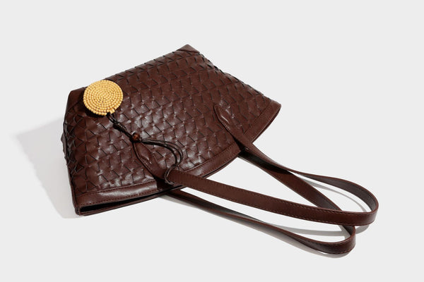 Large leather-look tote bag with geometric woven emboss, double shoulder straps, and round woven cord charm in brown, detail