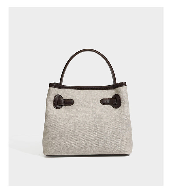 Small structured beige canvas top-handle bag with dark brown leather-look trim, silver turn-lock hardware, and detachable