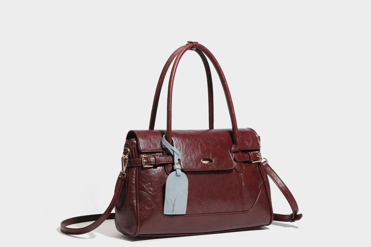 Structured glossy leather-look satchel bag with flap closure, gold-tone buckle accents, double top handles, detachable