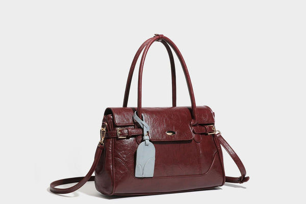 Structured glossy leather-look satchel bag with flap closure, gold-tone buckle accents, double top handles, detachable