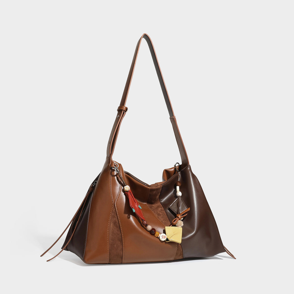 Two-tone black and brown leather-look slouchy shoulder bag with beaded tassel charm and silver-tone hardware, front view